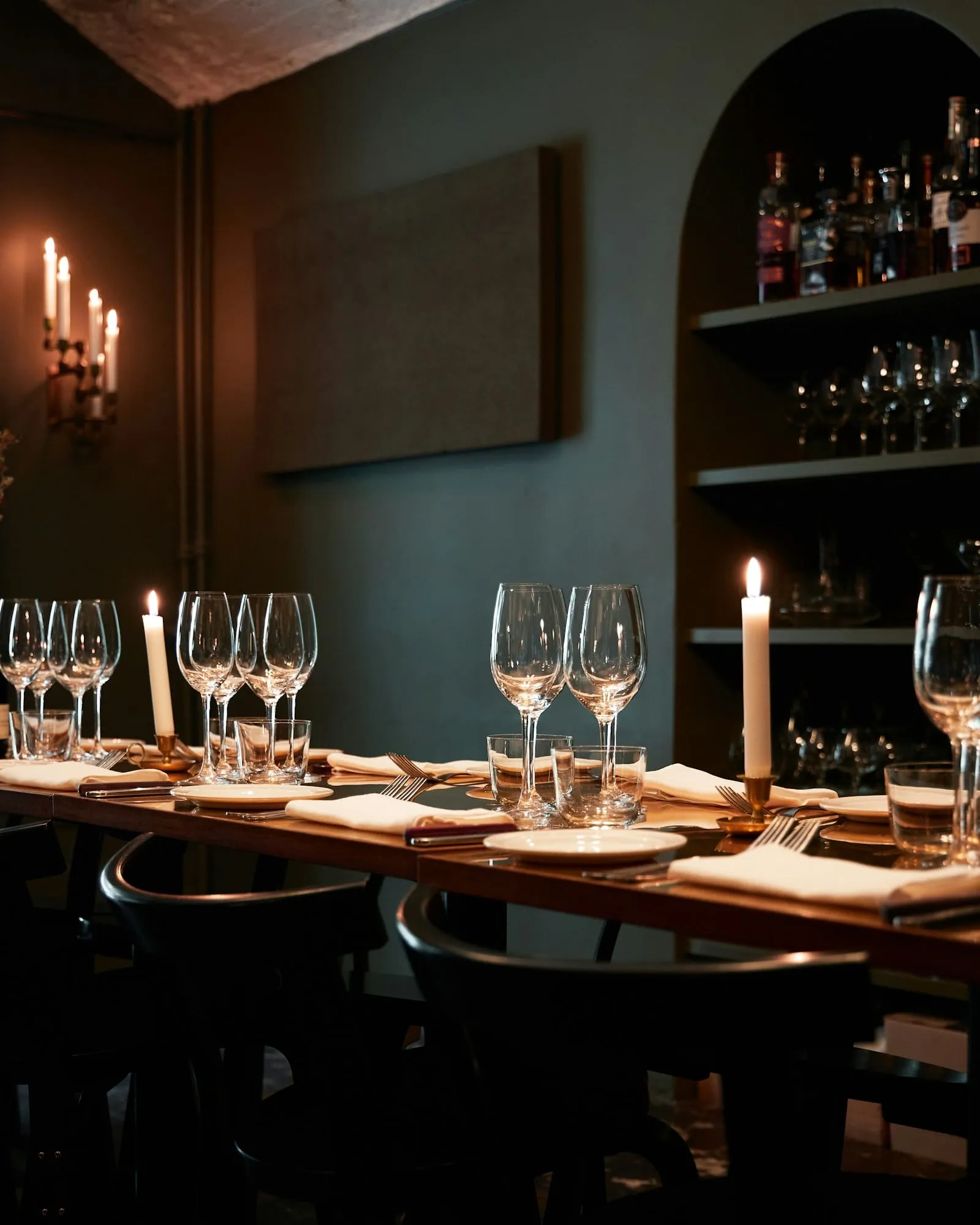 A narrow candlelit room set with wine glasses under an arched window