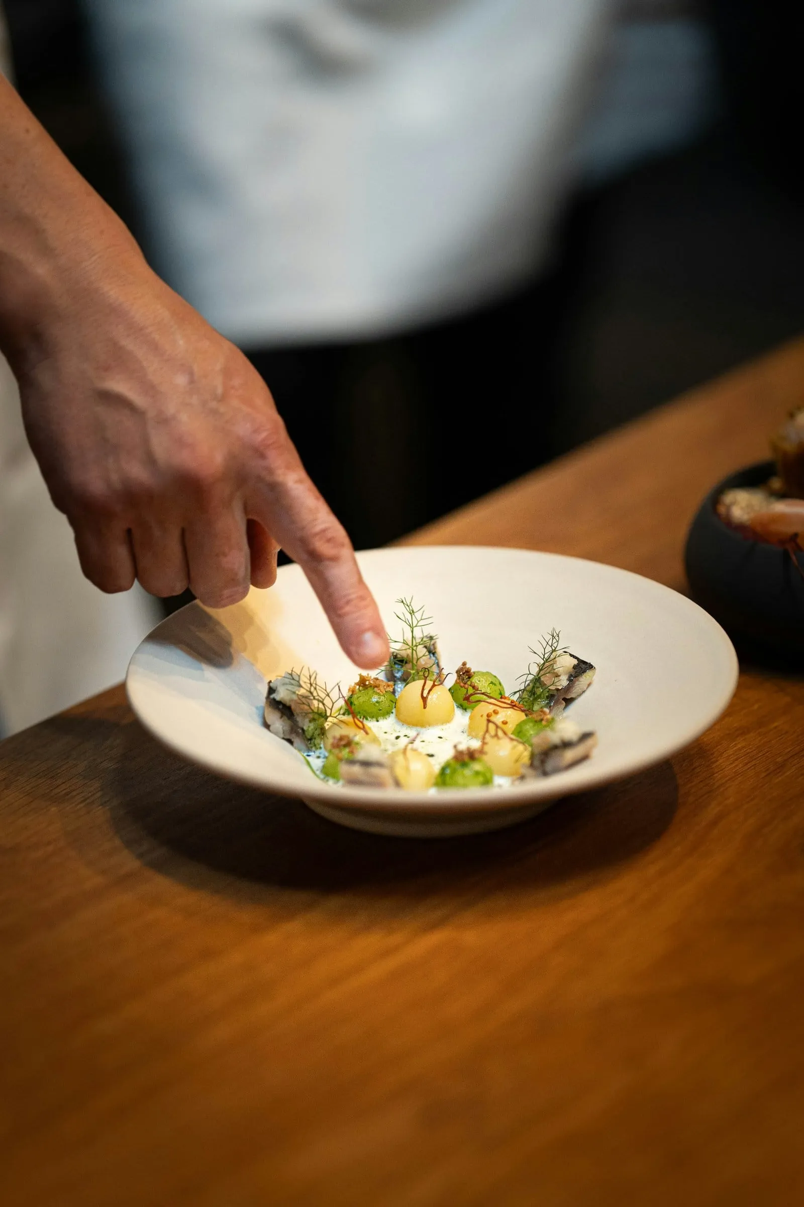 A plate of crudo being finished with herbs
