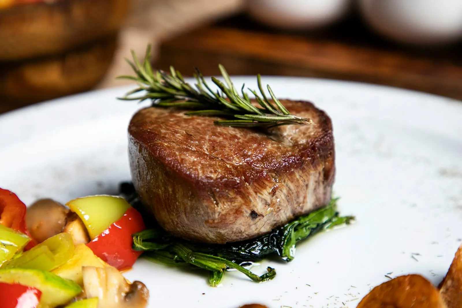 A filet topped with rosemary beside colorful vegetables