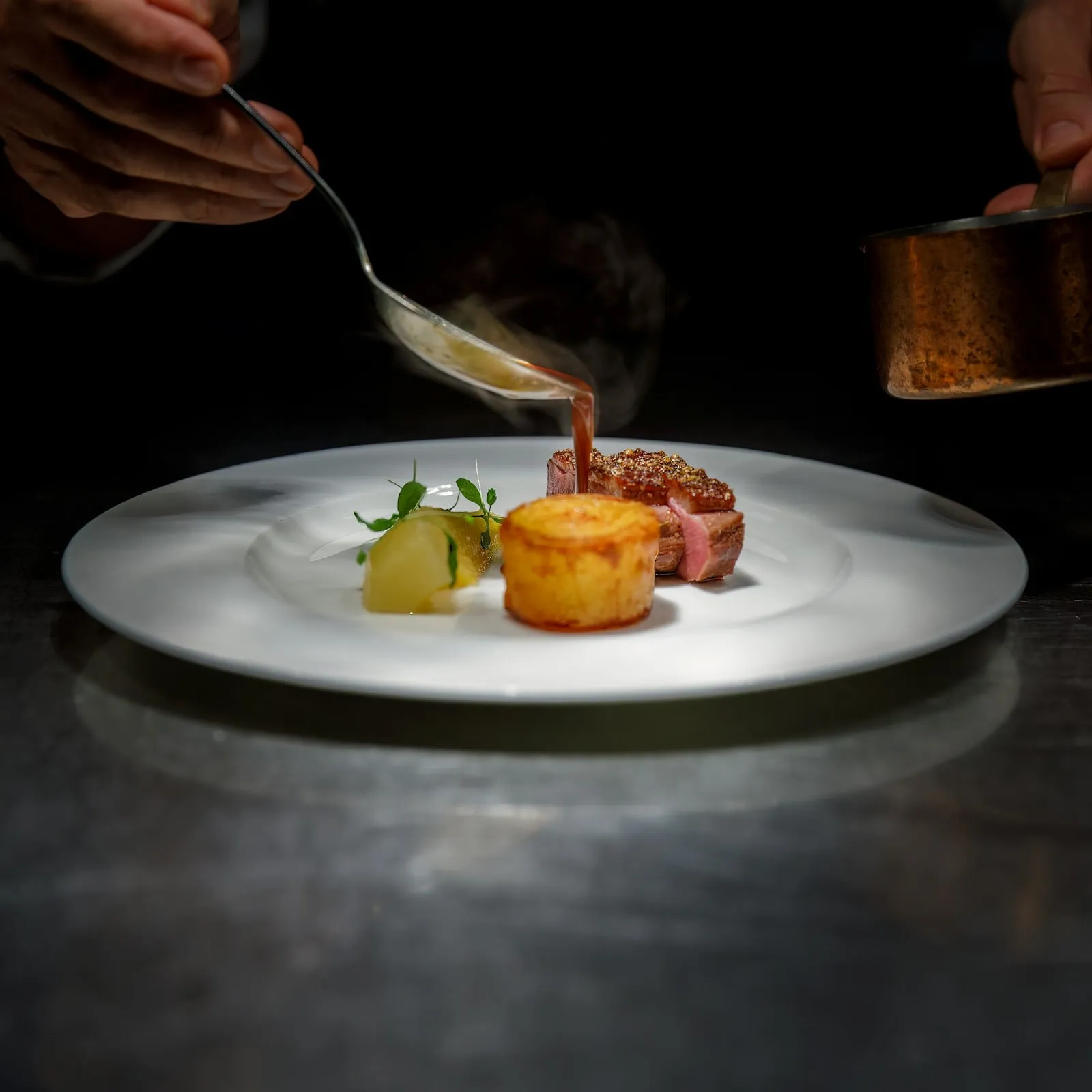 A sauce being poured over a course on a white plate