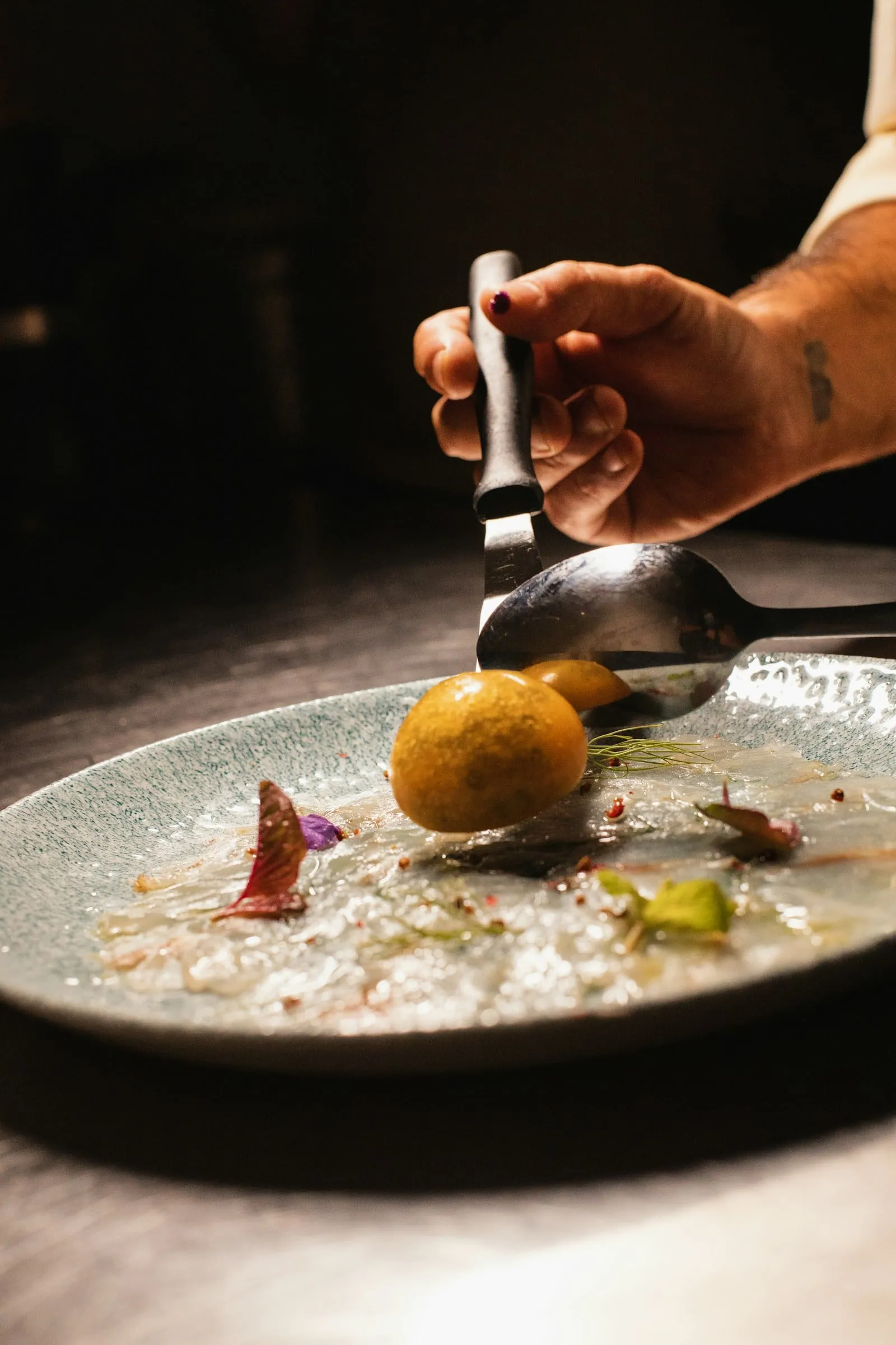 Sauce being spooned beside a small dish in low light