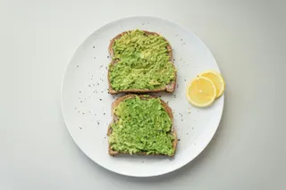 Two slices of avocado toast with a lemon wedge