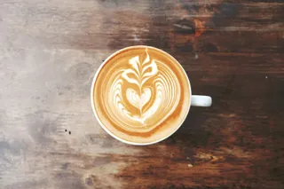 A cappuccino with a leaf of latte art on a wooden table
