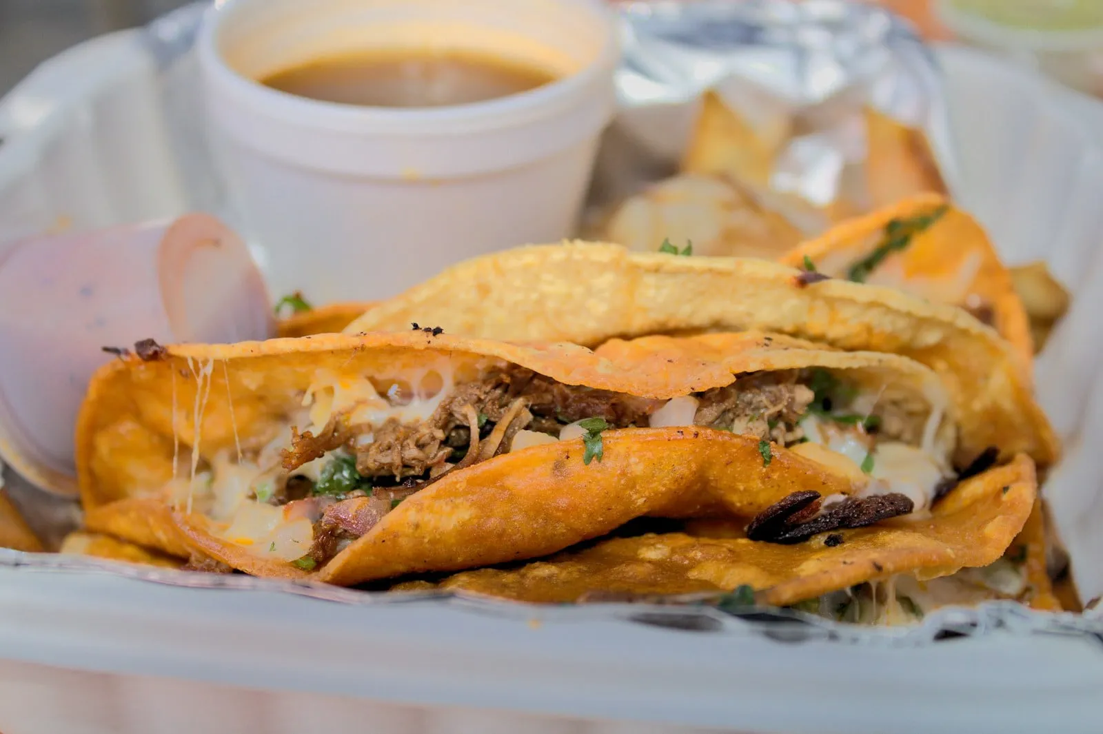Birria tacos in a tray with a cup of consomé