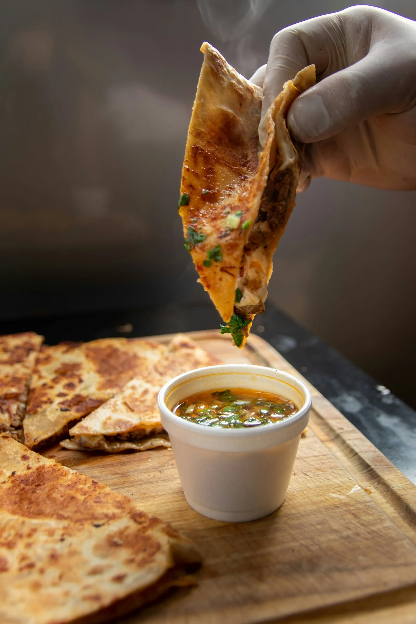 A birria taco being dipped into a cup of consomé