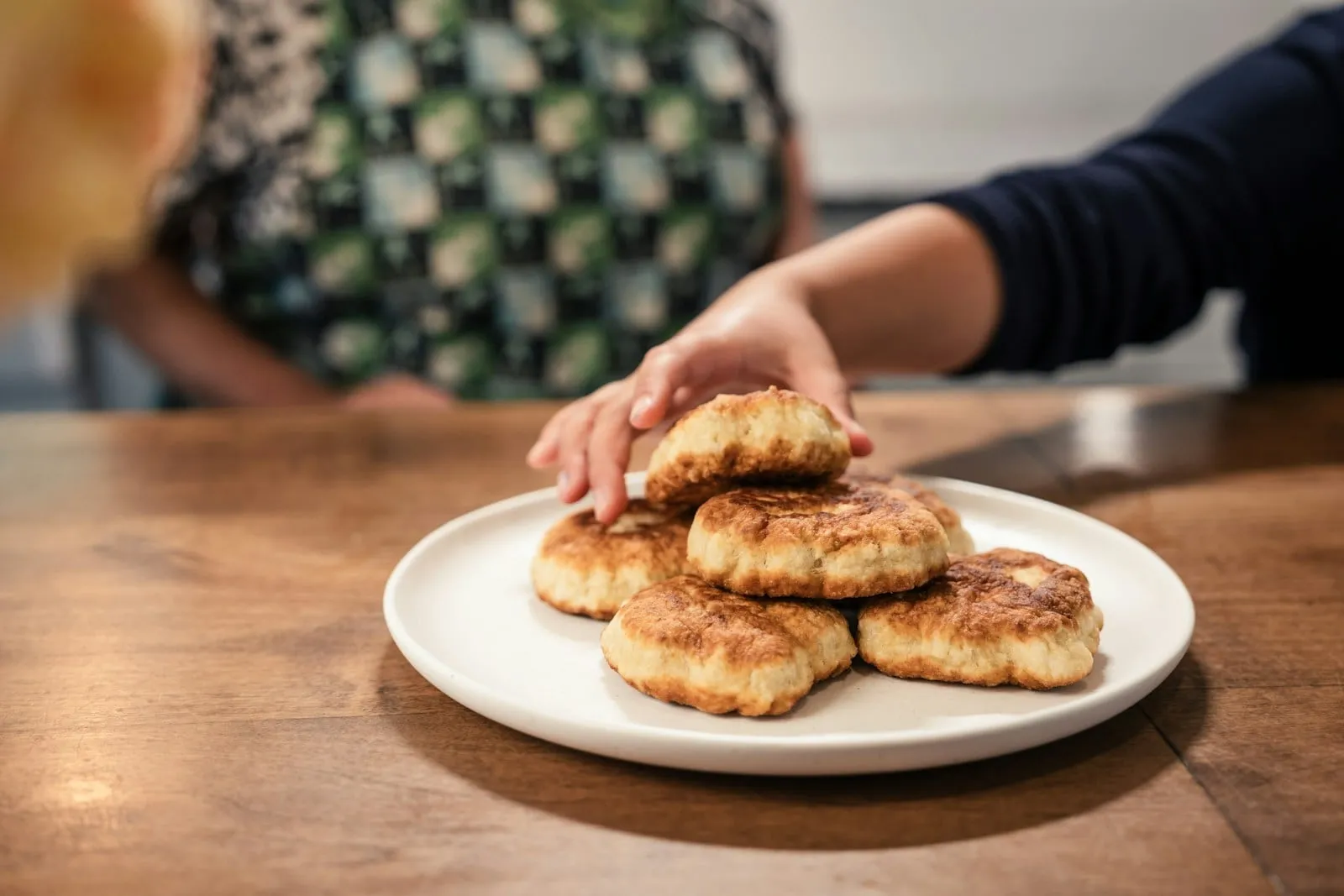 A hand reaching for a warm biscuit on a plate