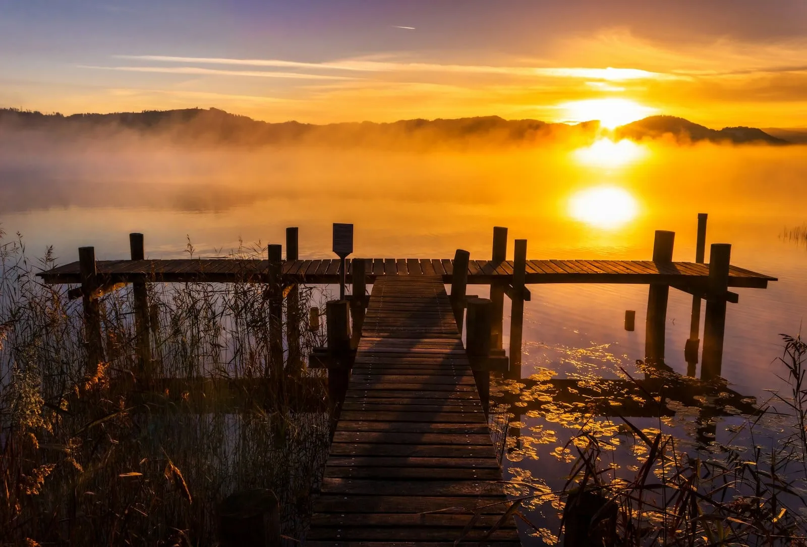 The sun setting over a misty lake behind an old wooden dock