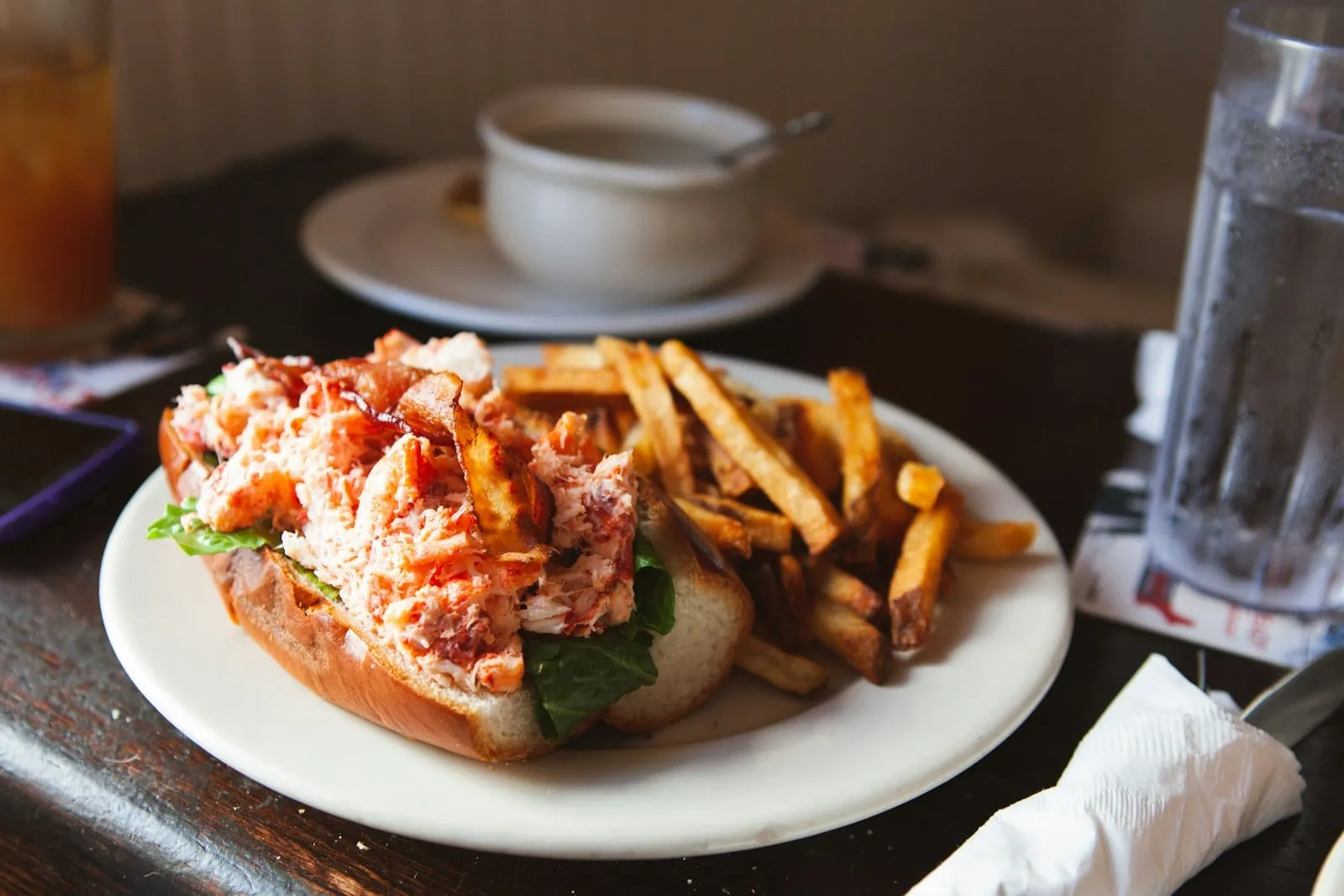 A lobster roll with fries on a white plate