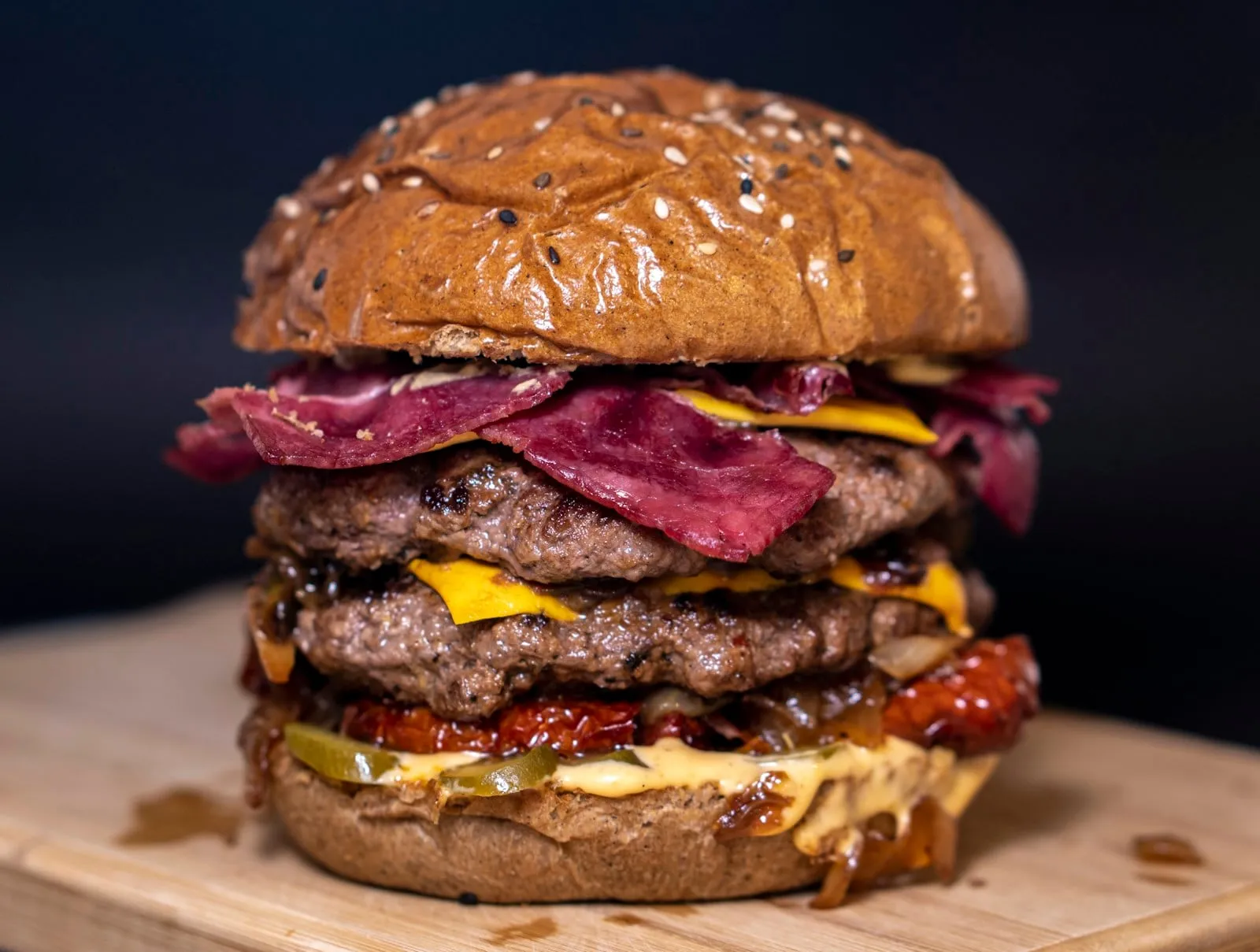 A triple cheeseburger with bacon on a wooden board