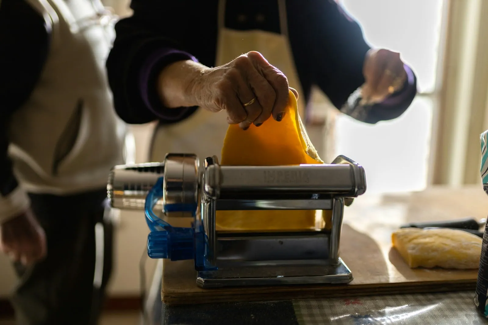 A cook rolling dough through a hand-cranked pasta machine